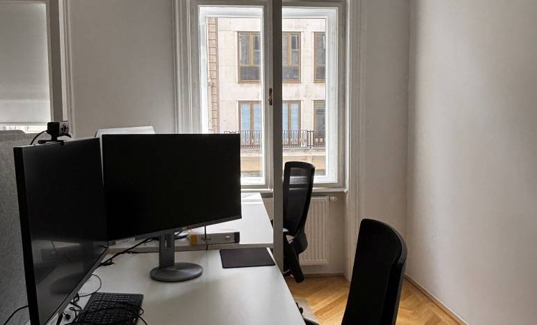 Einzelner Arbeitsplatz mit zwei Bildschirmen und Blick auf einen Wiener Altbau gegenüber